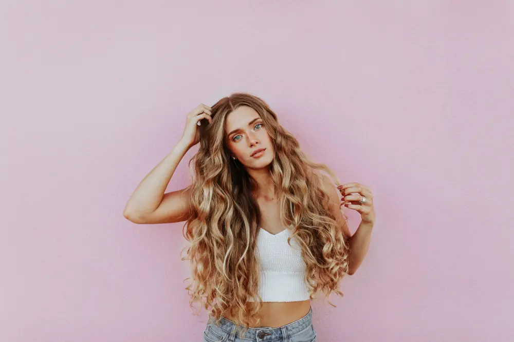 Castellano-Blog-Mar20 Woman with long curly hair wearing a crop tank and jeans in fron of pink background.