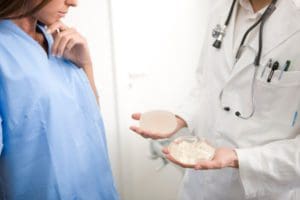 Doctor holding two different breast implants while female patient examines them.