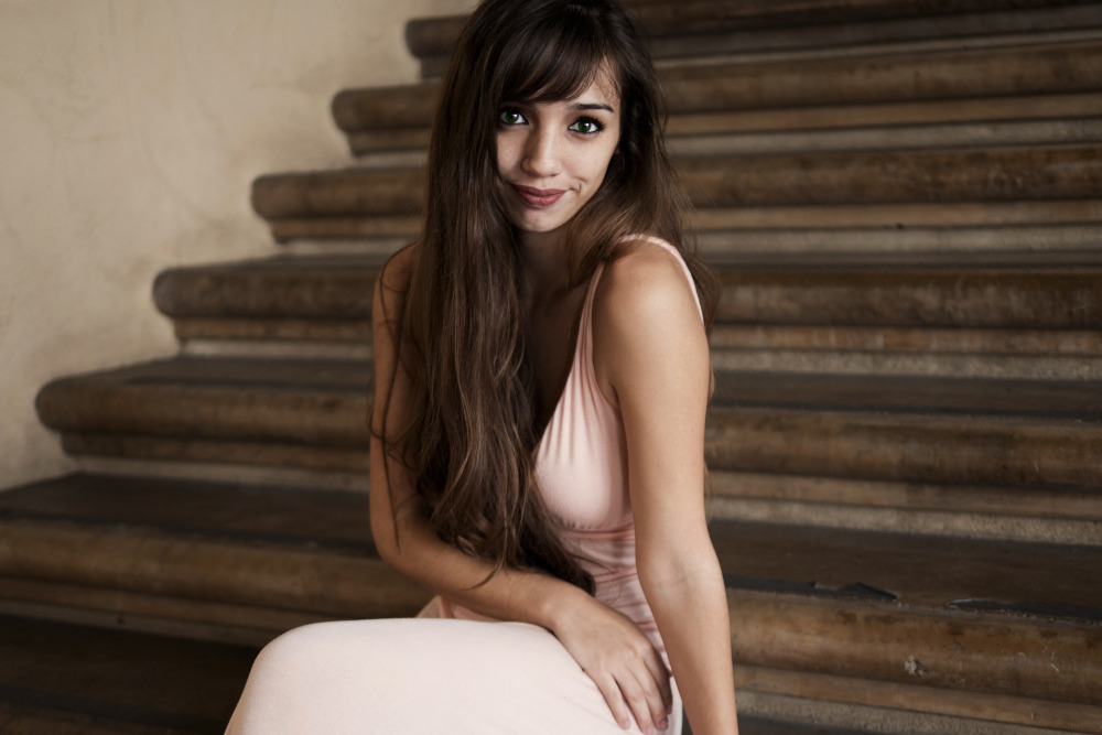 Woman in a light pink gown sitting on cement stairs.