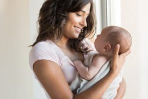 Portrait of a woman with lond dark straight hair holding her newborn baby.