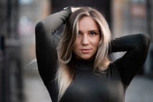 Considering breast implant options. Woman in black long-sleeved mock neck shirt holding up her long hair.