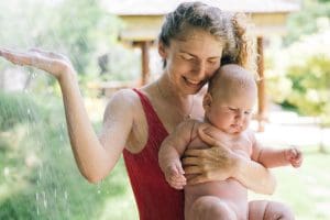 A joyful mother and her baby enjoy an outdoor shower, embracing summer fun and togetherness.